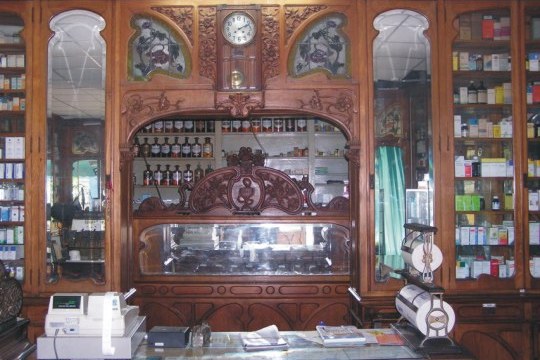 Taulell modernista d'una farmàcia amb rellotge i vitrines de fusta